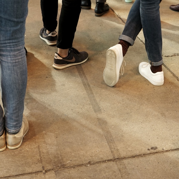 Mehrere Personen stehen beisammen, das Foto zeigt die Füße der Gruppe. Eine Person hat die Beine überkreuz.